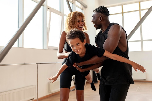 Afrikaans-Amerikaans gezin in sportkleding houdt en draagt zoon in de lucht en speelt in de sportschool