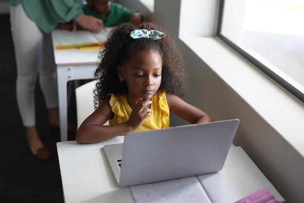 Afrikaans-Amerikaanse basisschoolmeisje met een laptop aan het bureau in de klas tijdens de computerles