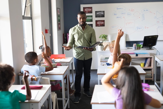 Afrikaans-Amerikaanse jonge mannelijke leraar met dossier staande bij multiraciale studenten met de hand omhoog. onveranderd, onderwijs, leren, jeugd, onderwijs, beroep en schoolconcept.