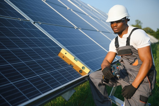 Afrikaans-Amerikaanse man in veiligheidshelm en bril trekt moeren aan op zonnepanelen met een schroevendraaier Bekwaam technicus die gereedschap gebruikt tijdens het uitvoeren van onderhoudswerk op het station