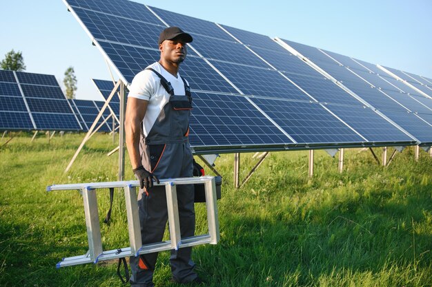 Afrikaans-Amerikaanse man in witte helm en grijze overalls die tussen rijen zonnepanelen staat