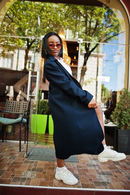 Afrikaans chique zakenmeisje in jas en zonnebril. Modieus straatportret van Afro-Amerikaanse vrouw.
