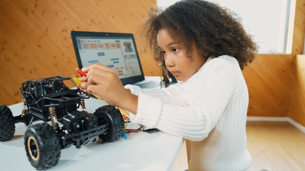 Afrikaans meisje bouwt een robotwagen met behulp van draden met behulp van een laptop Eruditie