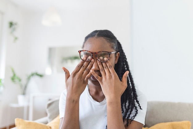 Afrikaans meisje met een bril wrijft in haar ogen, lijdt aan vermoeide ogen, concept van oogziekten