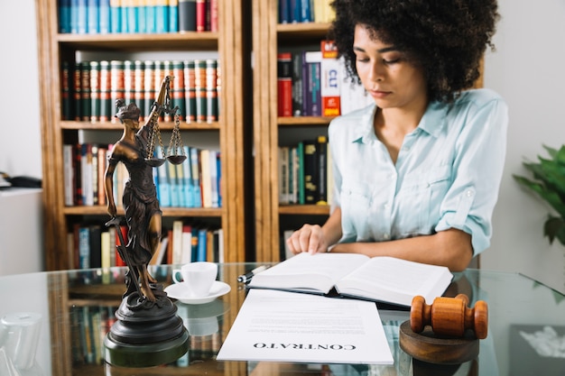 Foto afrikaanse amerikaanse jonge vrouw met boek aan tafel met beker en document