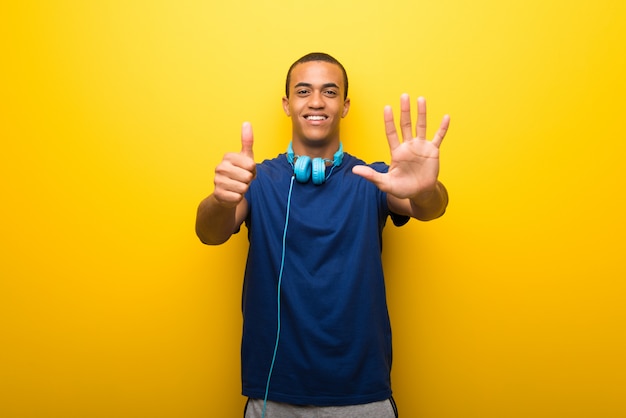 Afrikaanse Amerikaanse mens met blauwe t-shirt op gele achtergrond die zes met vingers telt