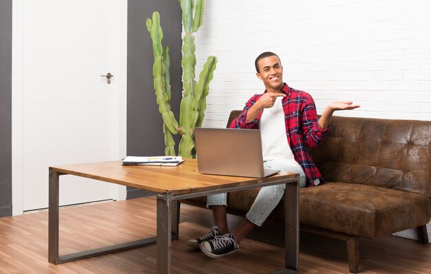 Afrikaanse Amerikaanse mens met laptop in de woonkamerholding copyspace denkbeeldig op de palm om een advertentie op te nemen