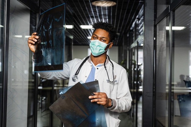 Afrikaanse arts onderzoekt röntgenfoto's in een medische kliniek Zwarte student met medisch masker bestudeert en kijkt naar ct-scans