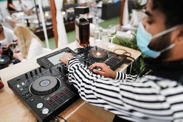 Foto afrikaanse dj die muziek speelt in de cocktailbar buiten terwijl hij een gezichtsmasker draagt - focus op de rechterhand