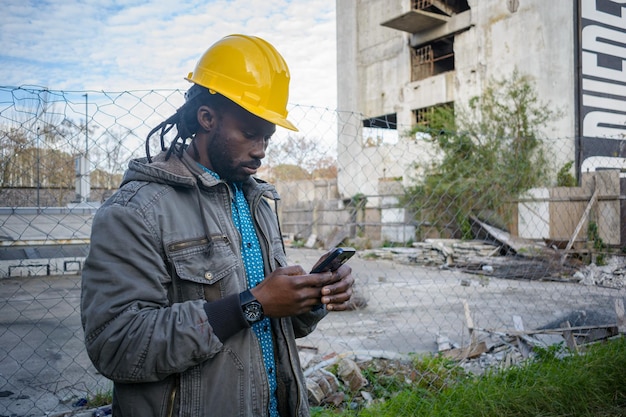 afrikaanse etniciteit bouwer man op bouwplaats sms'en op telefoon