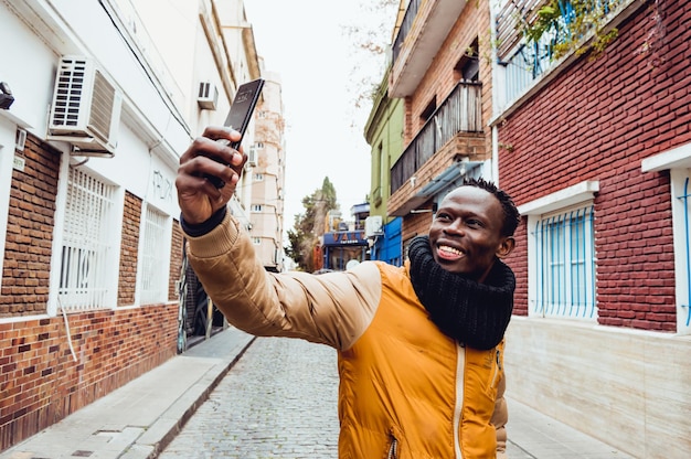 Afrikaanse etnische man die glimlachend midden op straat staat en een selfie maakt met zijn telefoon