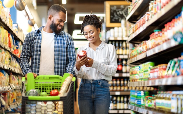 Afrikaanse familie die voedsel koopt in de supermarktwinkel die de kar duwt en samen boodschappen kiest. Tevreden klanten. Zwart Paar In Kruidenieropslag. Lege ruimte voor tekst