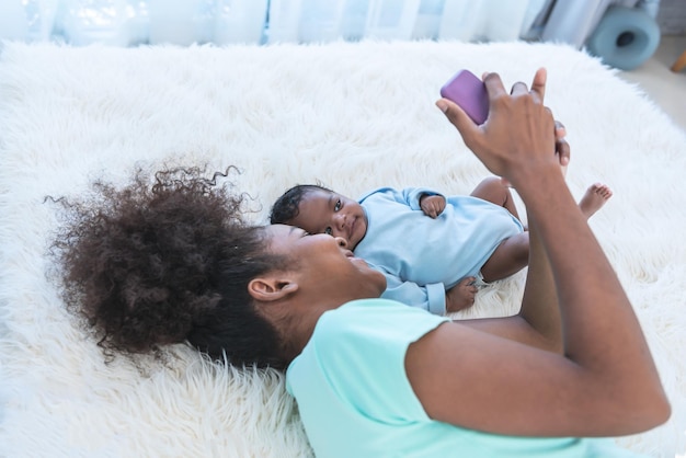 Afrikaanse familie Moeder en baby pasgeboren zoon liggend op wit bed en kijken naar mobiele telefoon