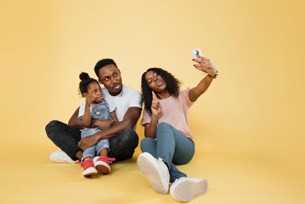 Afrikaanse familie van drie zittend op de vloer met smartphone terwijl ze foto's van hen maken met tongen