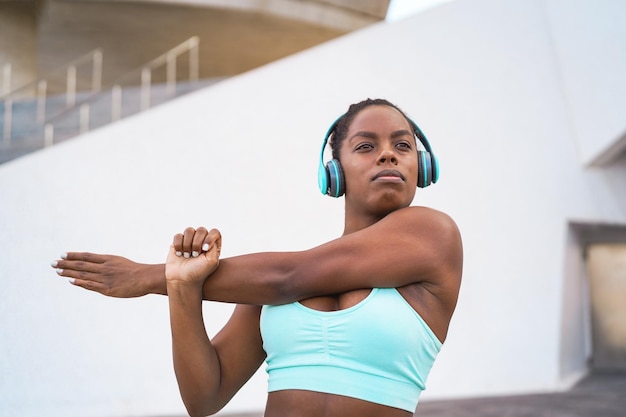 Afrikaanse fitte vrouw die muziek luistert met een koptelefoon terwijl ze zich uitstrekt voor de trainingsroutine buiten Sport, fitness en een gezonde levensstijl concept Focus op gezicht