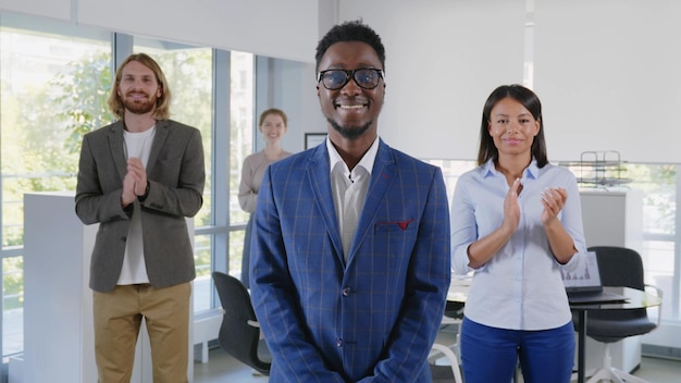 Afrikaanse jonge baas die naar de camera glimlacht met een divers team dat applaudisseert op de achtergrond