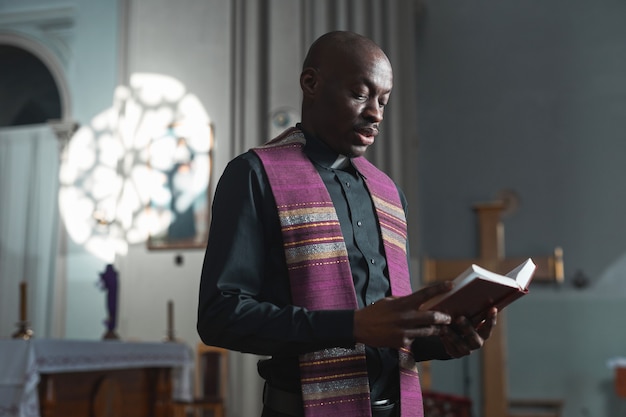 Afrikaanse jonge priester die de Bijbel leest tijdens de mis terwijl hij bij het altaar in de kerk staat