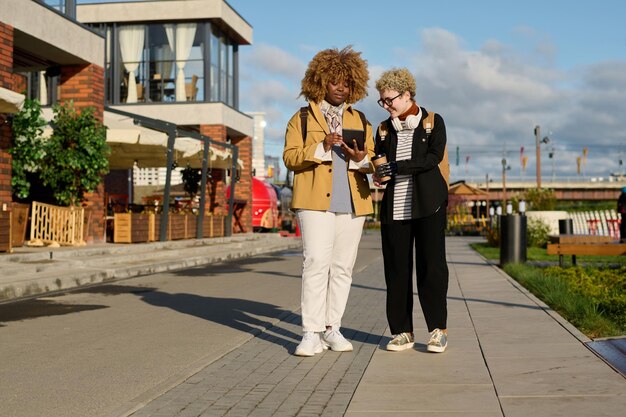 Afrikaanse jonge vrouw die digitale tablet buitenshuis gebruikt tijdens een wandeling met haar vriend in de stad