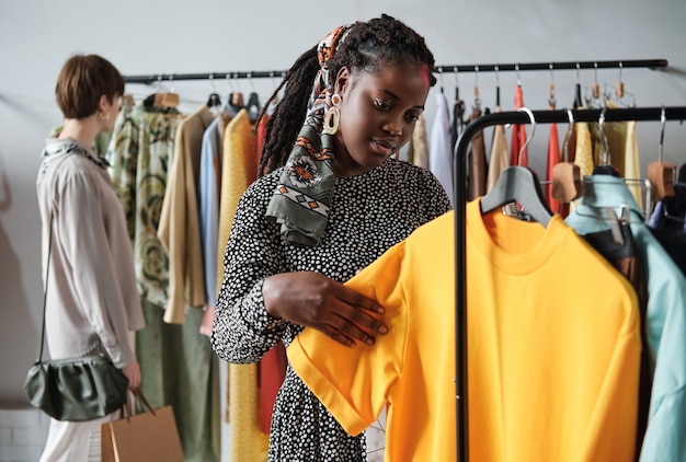 Afrikaanse jonge vrouw die nieuwe kleren voor zichzelf koopt in het winkelcentrum