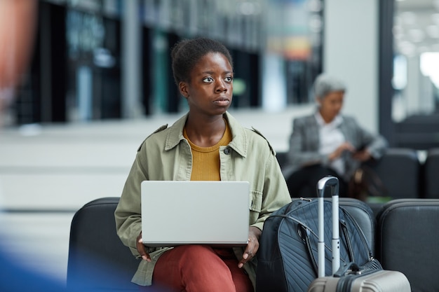 Afrikaanse jonge vrouw met behulp van haar laptop tijdens het zitten en wachten op haar vlucht op de luchthaven