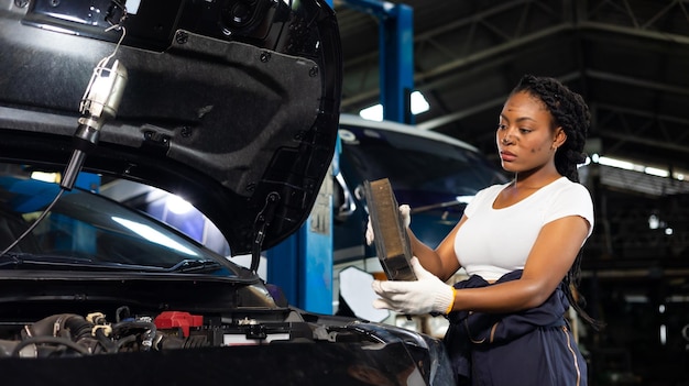 Afrikaanse jonge vrouwelijke automonteur die de luchtfiltermotor van de auto controleert en verandert in de garage voor serviceauto's Zwarte monteur die werkt in de autoservice- en onderhoudswerkplaats