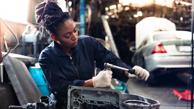 Afrikaanse jonge vrouwelijke automonteur die de motor van een auto controleert en repareert in de garage voor serviceauto's Zwarte monteur die werkt in de werkplaats voor autoservice en -onderhoud