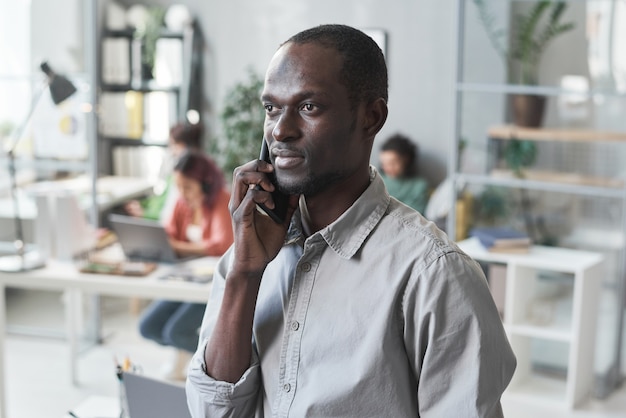 Afrikaanse jonge zakenman die op mobiele telefoon praat terwijl hij op kantoor werkt