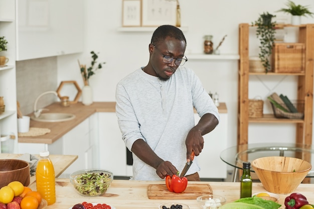 Afrikaanse jongeman die verse tomaat op snijplank snijdt voor salade in de keuken