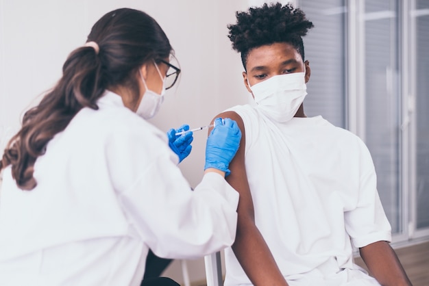 Afrikaanse jongen met gezichtsmasker wordt gevaccineerd tijdens coronavirus of covid-19 pandemie in het ziekenhuis, vaccinatieconcept