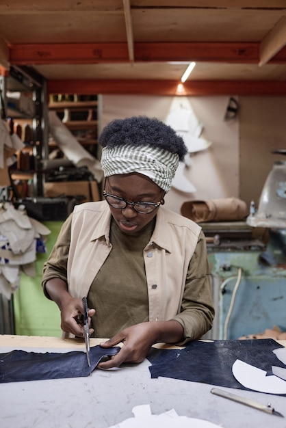 Afrikaanse kleermaker zit op haar werkplek en knipt stof met een schaar, ze naait kleding in de werkplaats