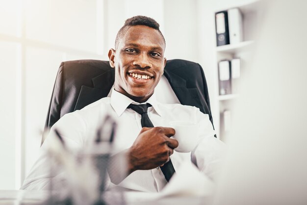 Afrikaanse lachende zakenman zit op kantoor tevreden met zijn werk.