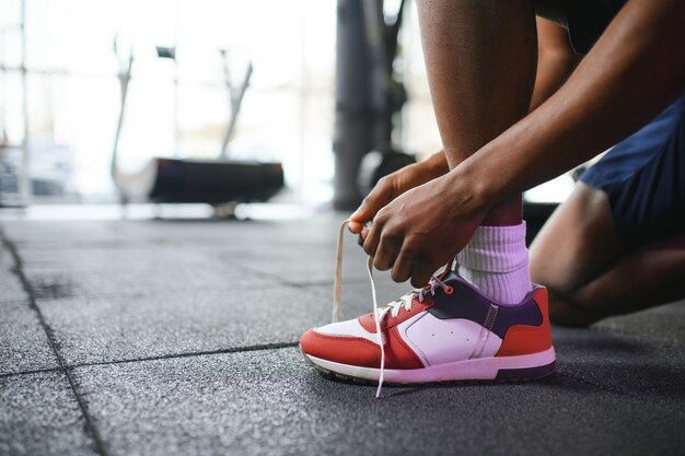 Afrikaanse man die schoenveters vastbindt aan een sneaker in de sportschool