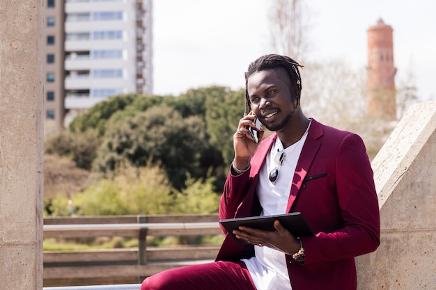 Afrikaanse man die tablet gebruikt en telefonisch praat