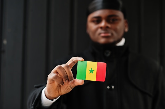 Afrikaanse man draagt zwarte durag houdt Senegal vlag bij de hand geïsoleerde donkere muur