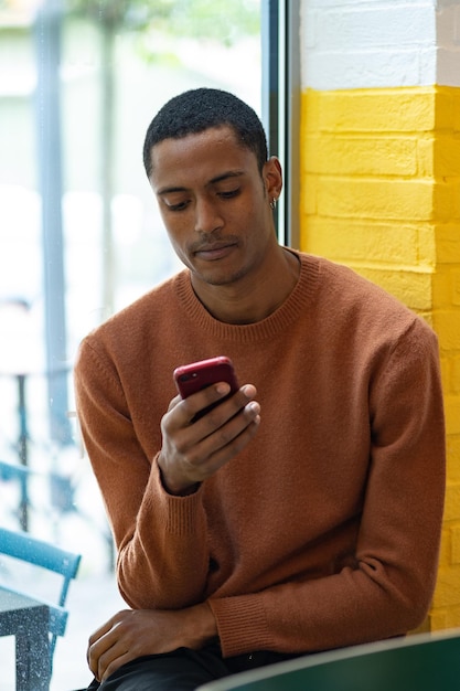 Afrikaanse man gebruikt zijn smartphone in een café gekleed in een trui draadloos internet