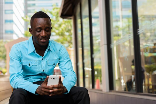 Afrikaanse man glimlachend en zittend tijdens het gebruik van mobiele telefoon