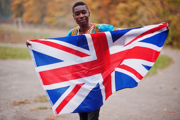 Afrikaanse man in het traditionele shirt van Afrika op herfst park met Groot-Brittannië vlag.