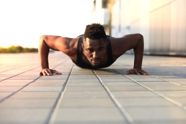 Foto afrikaanse man in sportkleding die plankpositie op het strand houdt tijdens het sporten buiten, bij zonsondergang of zonsopgang.