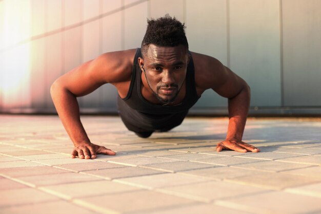 Afrikaanse man in sportkleding die plankpositie op het strand houdt tijdens het sporten buiten, bij zonsondergang of zonsopgang.