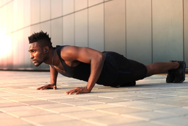 Afrikaanse man in sportkleding die plankpositie op het strand houdt tijdens het sporten buiten, bij zonsondergang of zonsopgang.