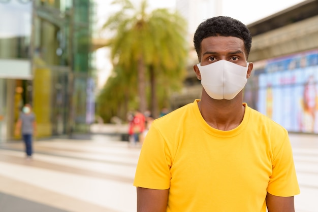 Afrikaanse man met geel t-shirt en gezichtsmasker ter bescherming tegen Covid-19 coronavirus buiten in de stad