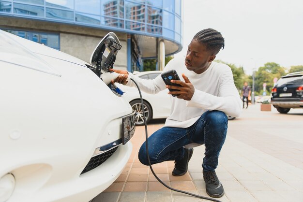 Afrikaanse man met laadkabel in de buurt van luxe elektrische auto.