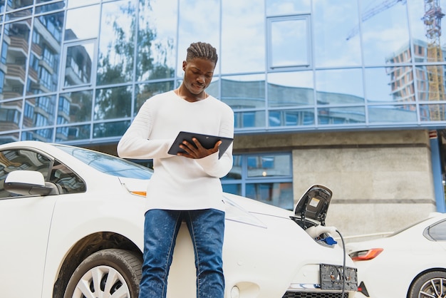 Afrikaanse man met laadkabel in de buurt van luxe elektrische auto.