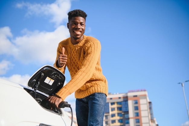 Afrikaanse man met laadkabel in de buurt van luxe elektrische auto.