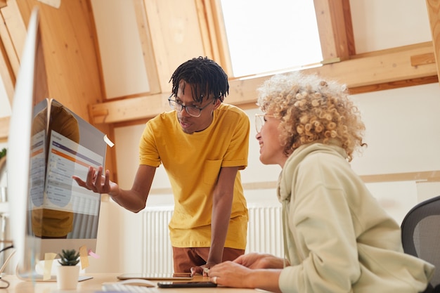 Afrikaanse man wijzend op de monitor van de computer en praat met de vrouw die ze nieuwe software op kantoor bespreken