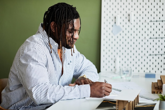 Afrikaanse man zit op zijn werkplek en maakt plannen voor een bouwproject