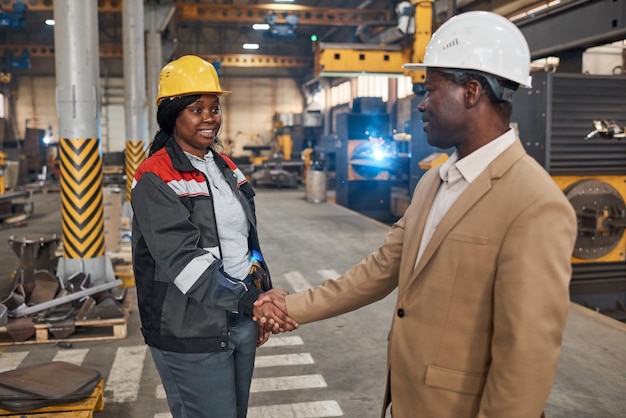 Afrikaanse manager in pak handen schudden met vrouwelijke werknemer in uniform om haar in fabriek in te huren