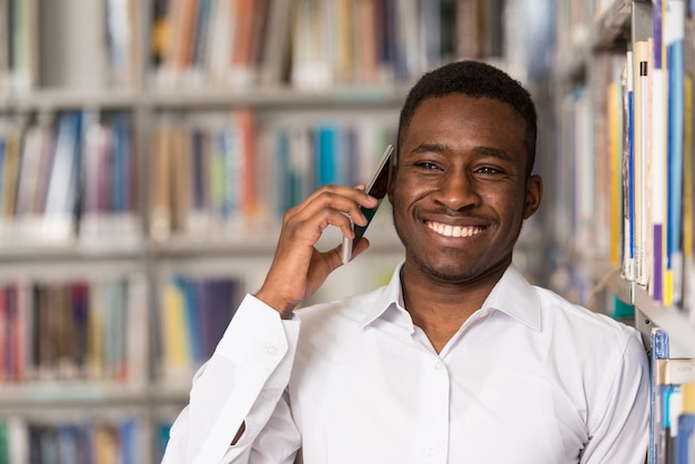 Afrikaanse mannelijke student praten aan de telefoon in bibliotheek ondiepe scherptediepte