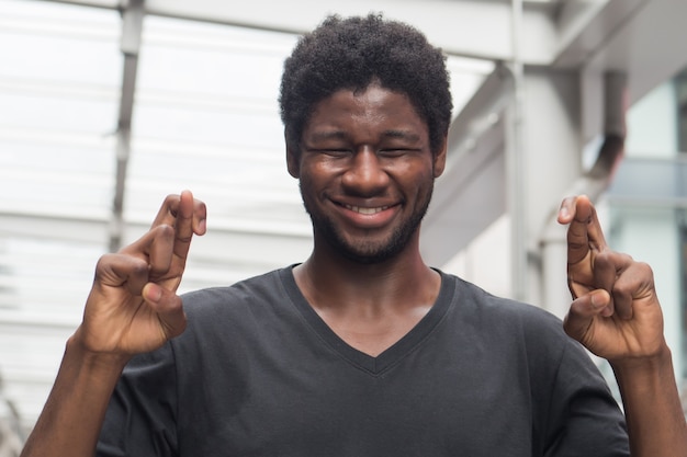 Afrikaanse mens die zijn vinger kruist; portret van de Afrikaanse man of zwarte man met gekruiste vinger, die geluk wenst, een wens voor fortuin of succes doet; afrikaans jonge volwassen man model