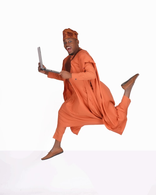 Afrikaanse Nigeriaanse man traditionele Yoruba kleding Agbada hoog springen met een laptop